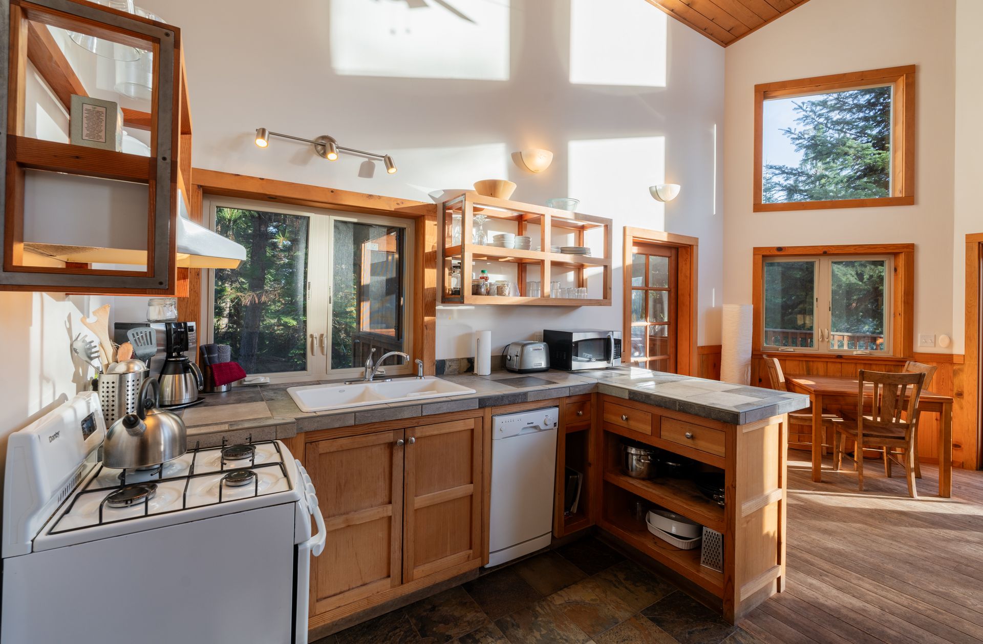 A kitchen with wooden cabinets , a stove , a sink , and a lot of windows.