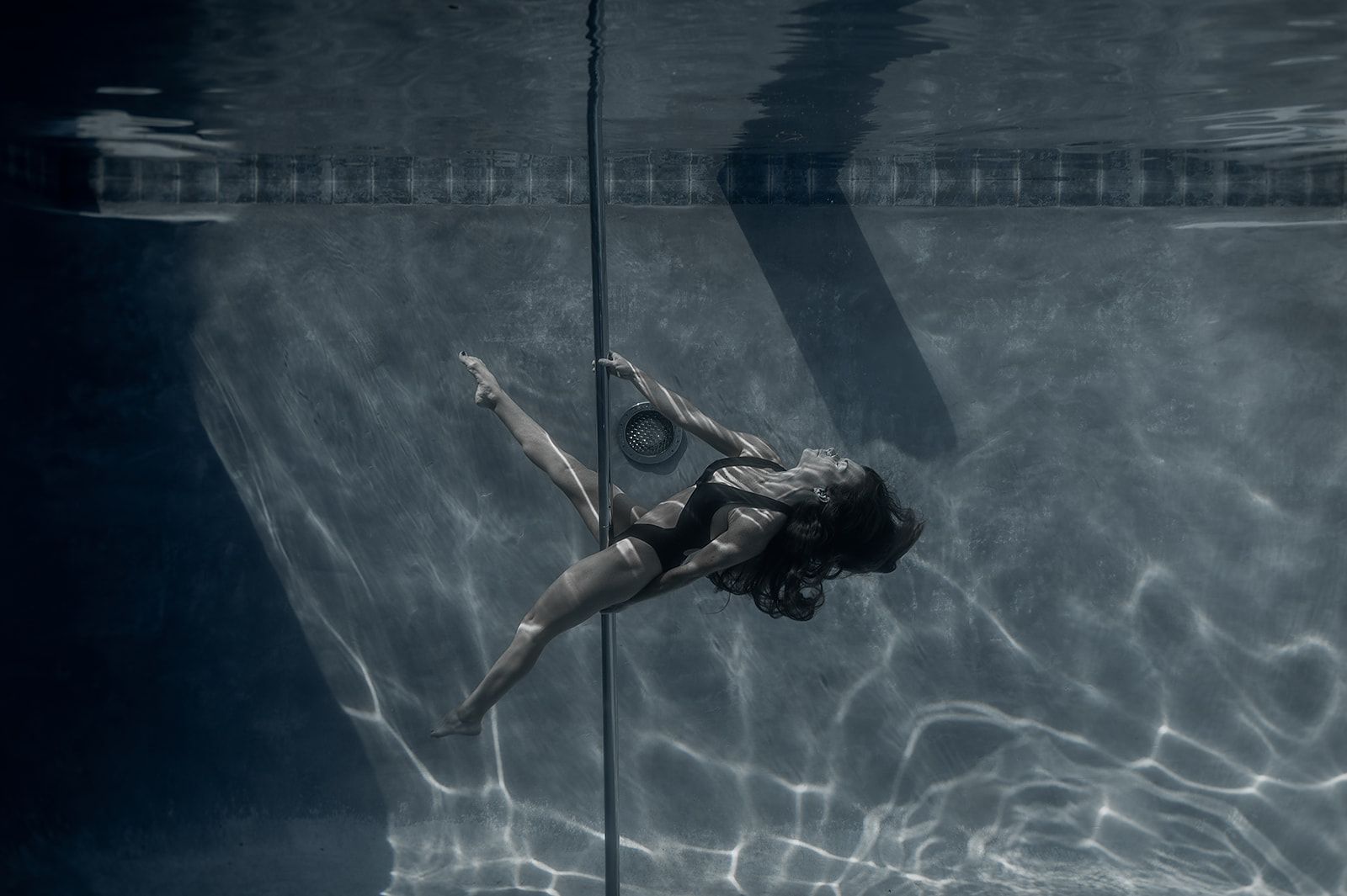 A woman is dancing pole dance underwater in a swimming pool.