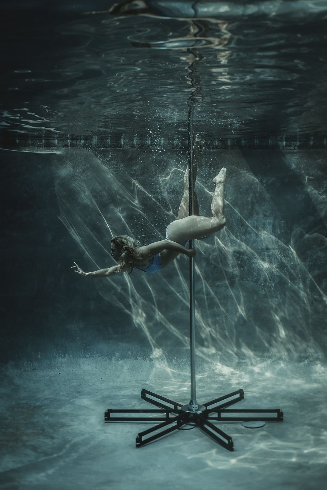 A woman is dancing on a pole underwater in a pool.
