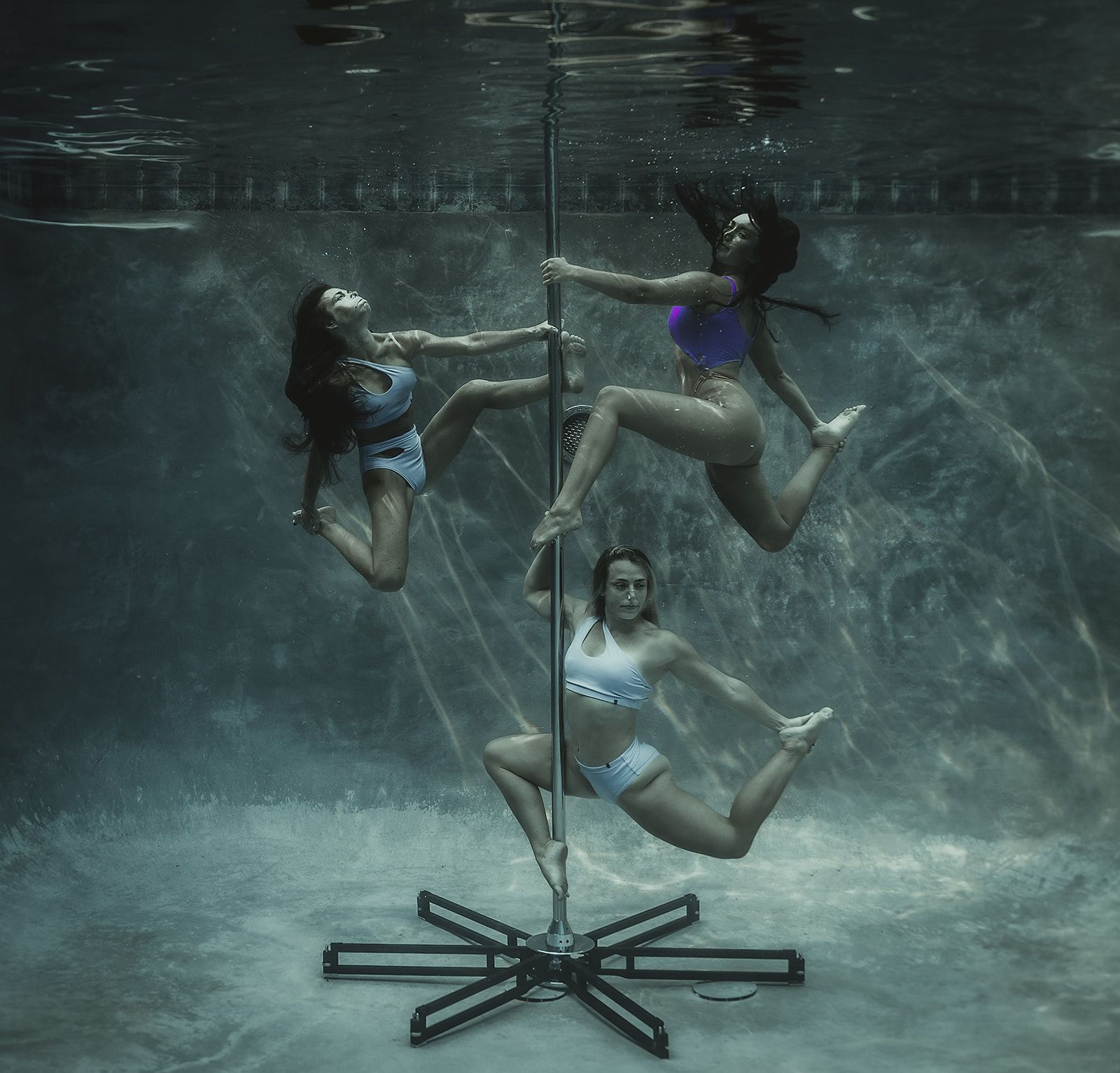 Three women are doing aerial acrobatics underwater in a pool