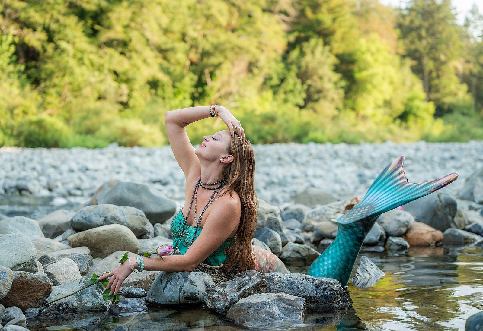 A woman in a mermaid costume is sitting on a rock in a river.