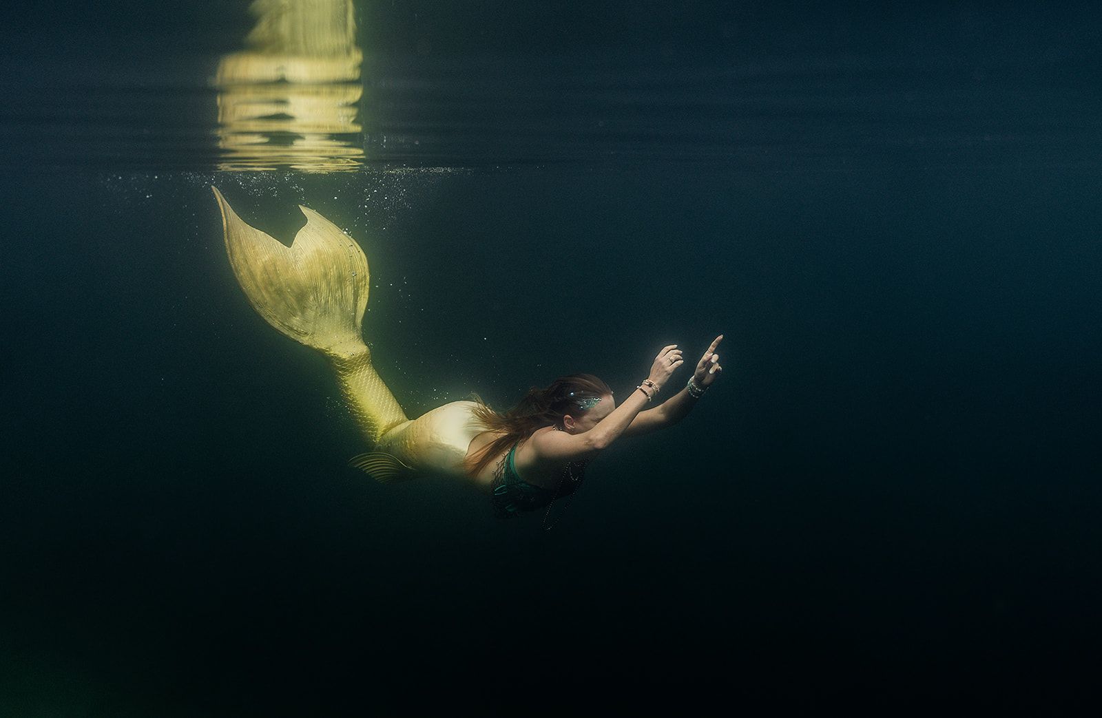 Mermaid with a golden tail swims underwater, arms outstretched.