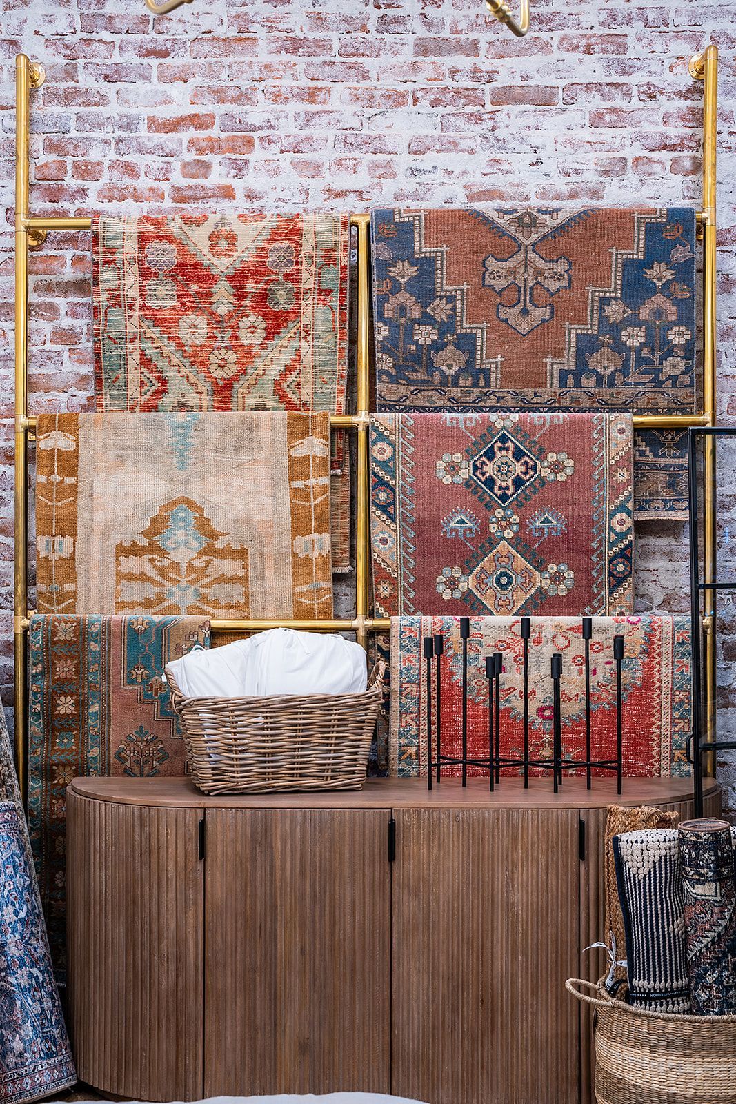 A bunch of rugs are stacked on top of each other on a shelf in front of a brick wall.