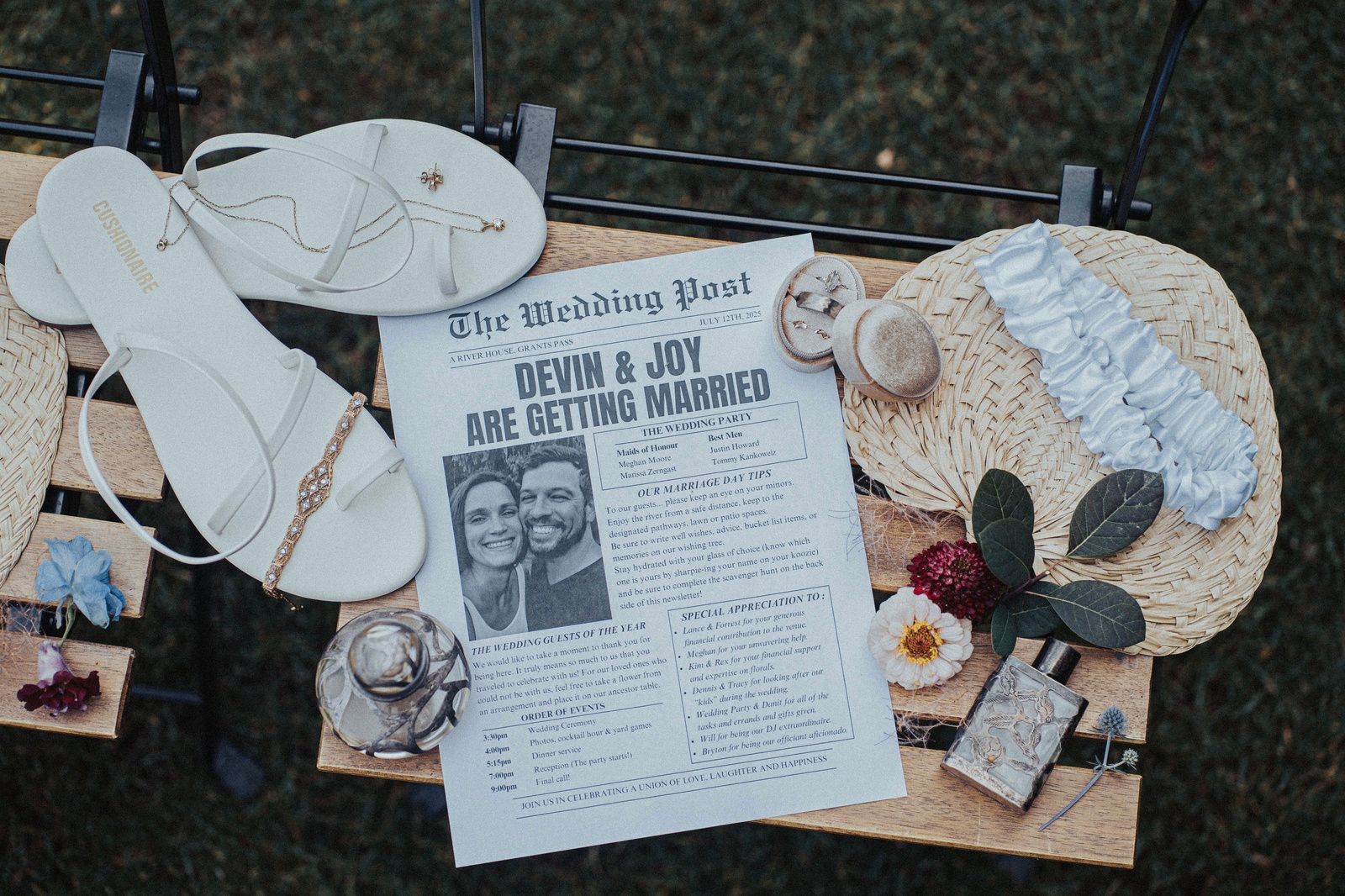 Wedding flat lay: newspaper announcement, sandals, fan, perfume, flowers, and garter on a wood and metal display.