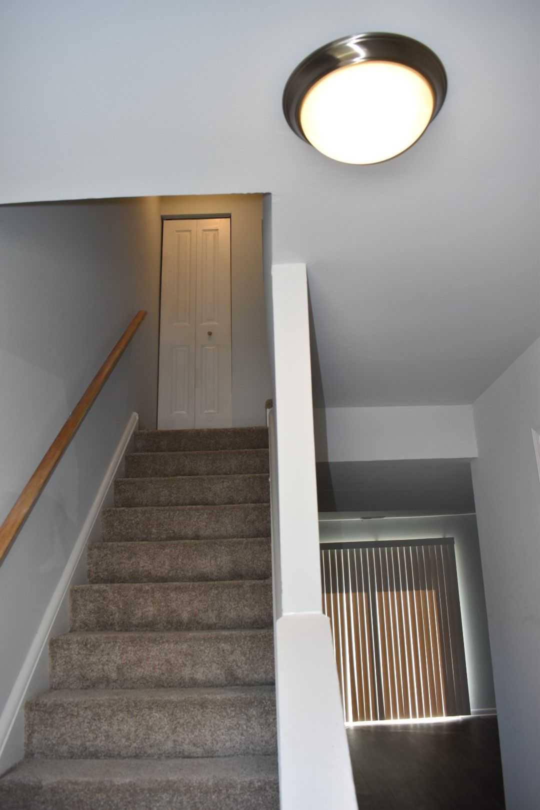 Carpeted staircase in a home hallway with a white ceiling light and a window with blinds below.