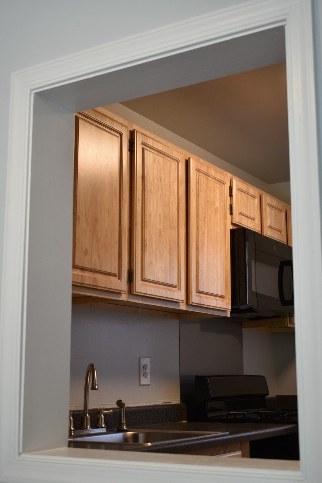 View into a kitchen with wood cabinets, dark countertops, and a sink under a doorway.