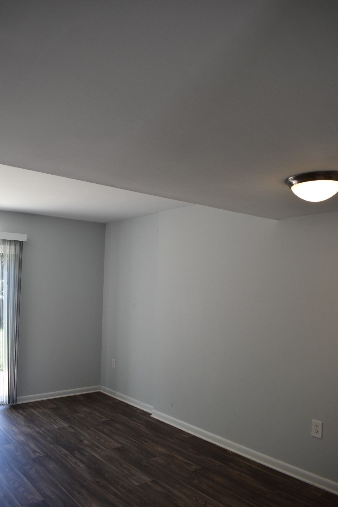Empty modern living room with gray walls, dark wood floors, and a ceiling light