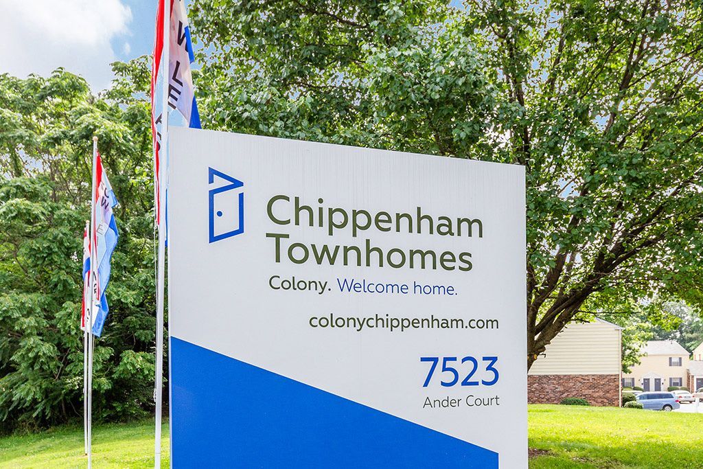 Chippenham Townhomes sign with blue logo and address, set beside trees and flags