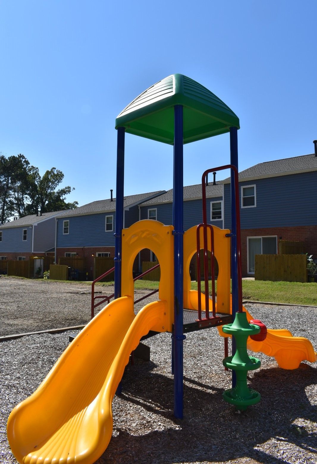 Colorful playground play structure with slide and climbing features in front of apartment buildings