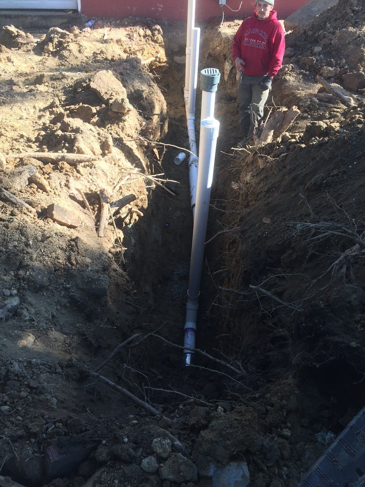 A man is standing in the dirt next to a pipe.