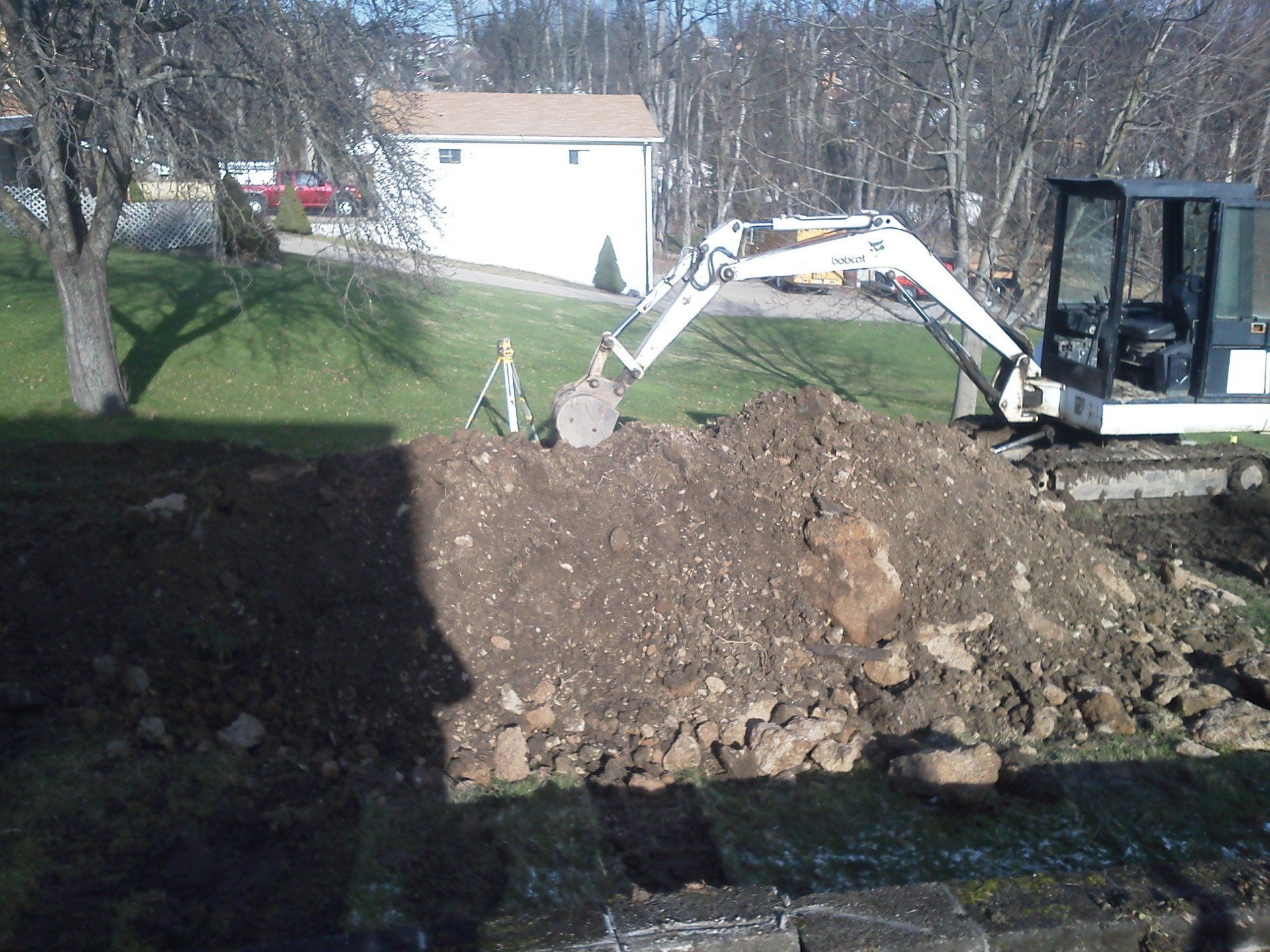 An excavator is digging a large pile of dirt in a yard