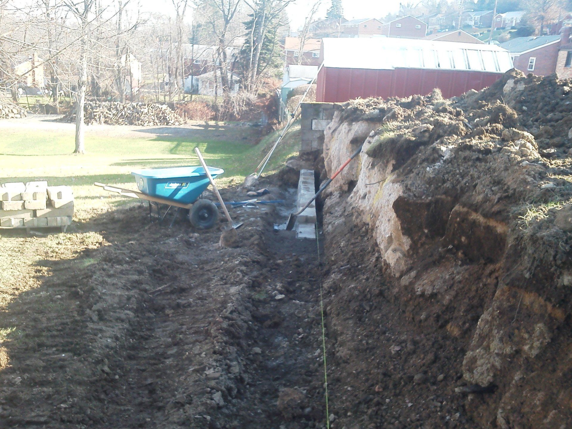 A blue wheelbarrow is sitting in a pile of dirt in front of a red barn