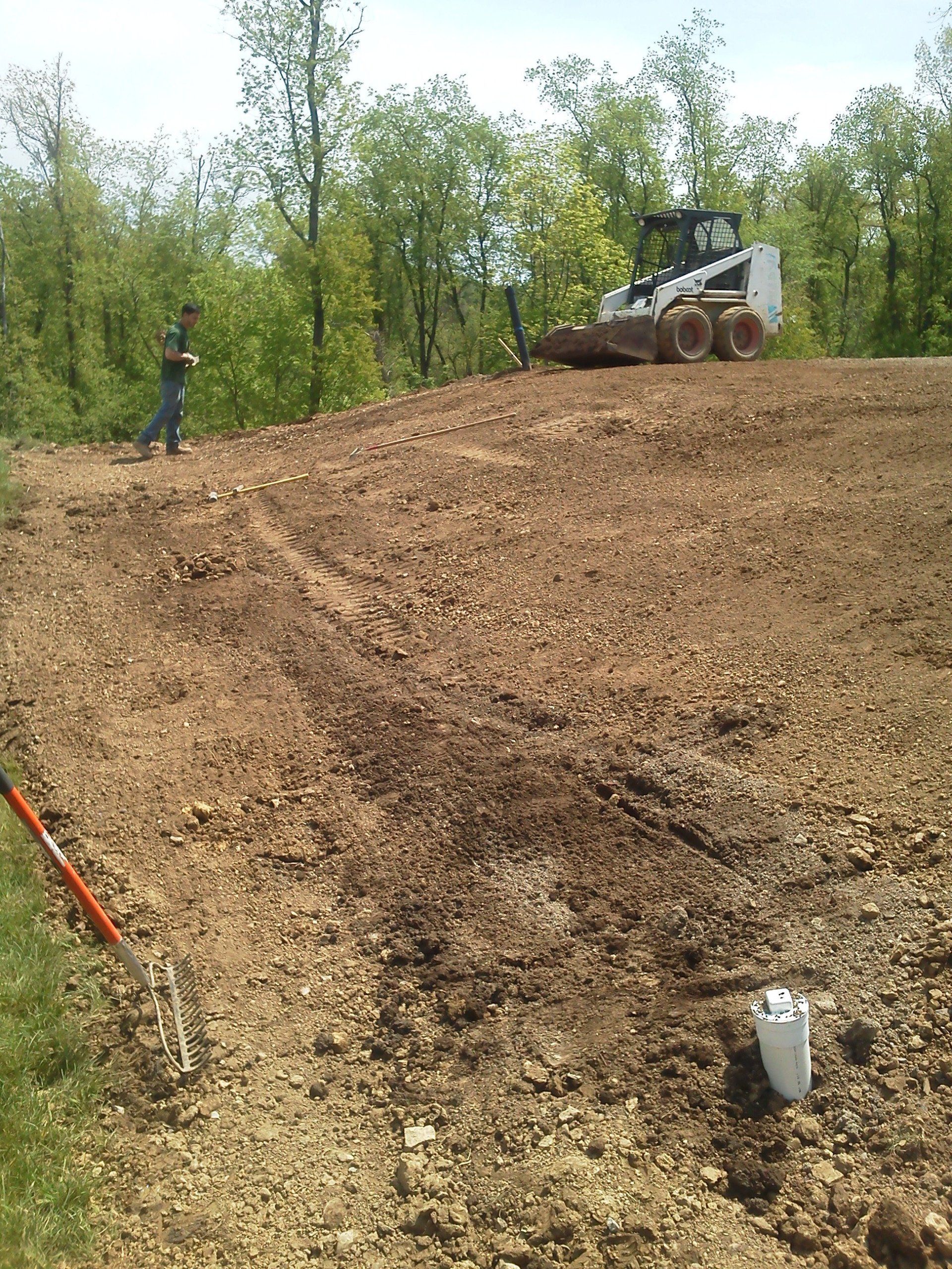 A man is standing on top of a dirt hill next to a bulldozer.