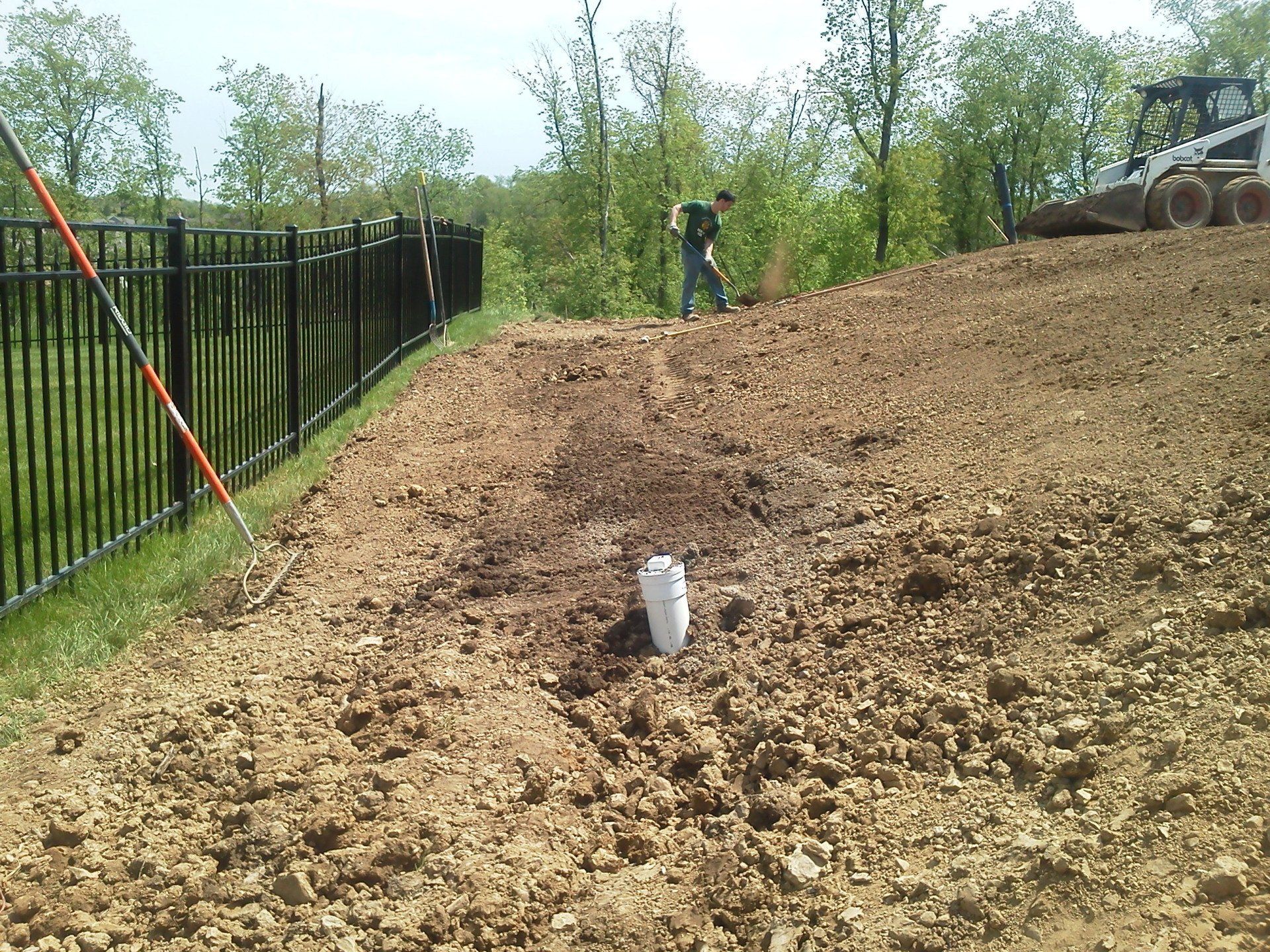 A man is working on a dirt hill with a fence in the background.
