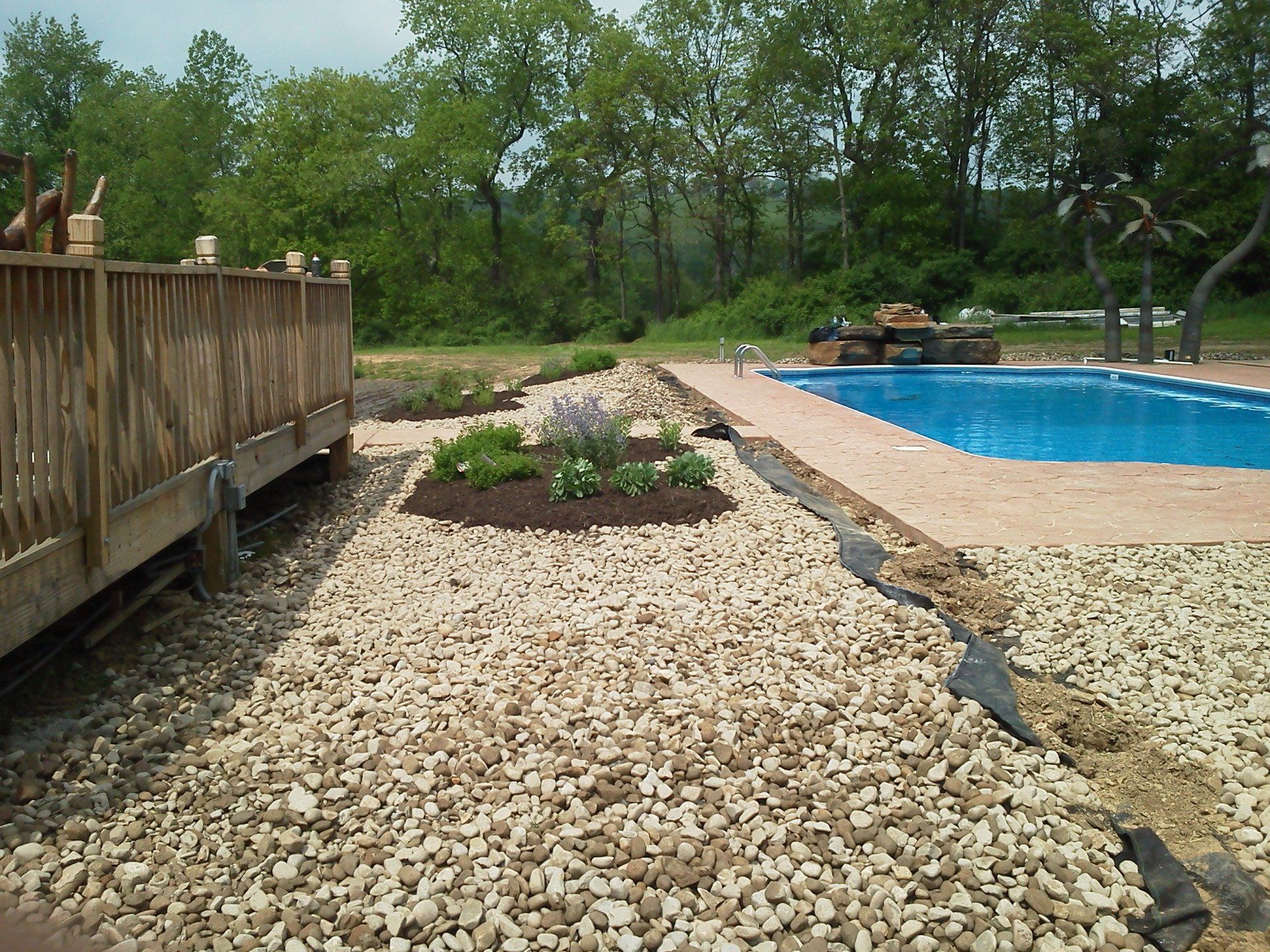 A swimming pool is surrounded by gravel and trees