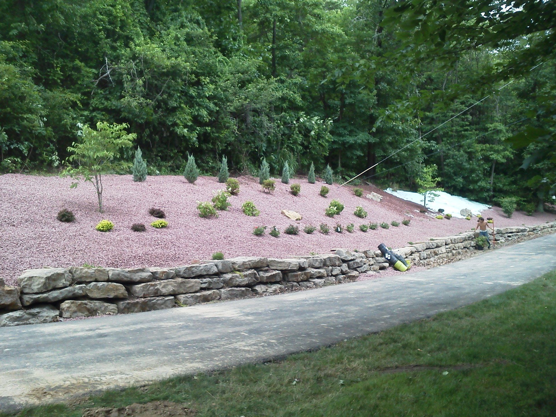 A stone wall surrounds a lush green hillside with trees and bushes.