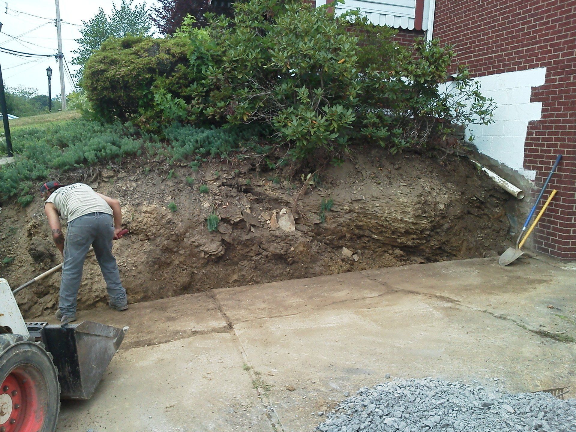 A man is digging in the dirt in front of a brick building.