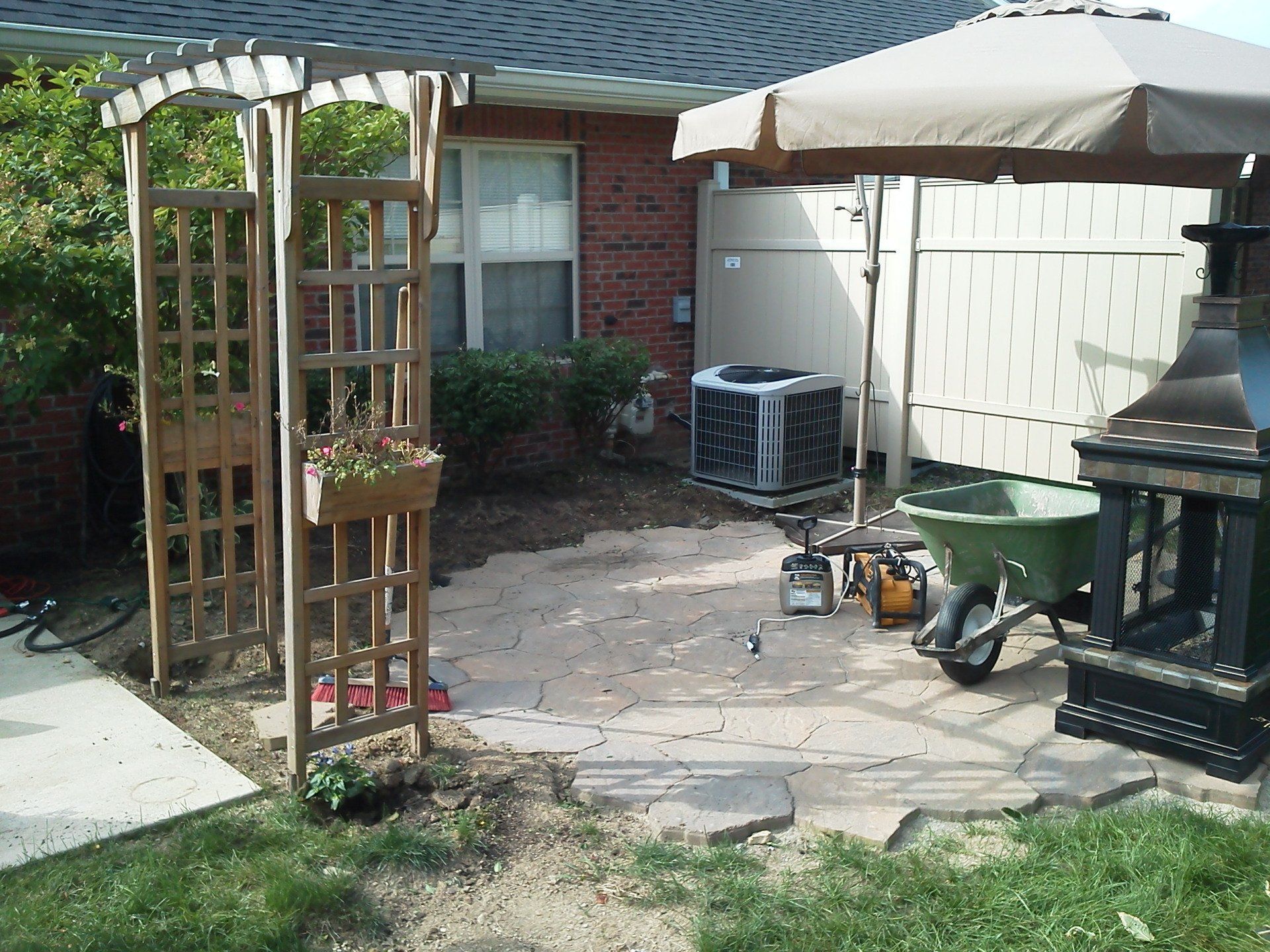 A patio with a wheelbarrow and an umbrella in front of a brick house