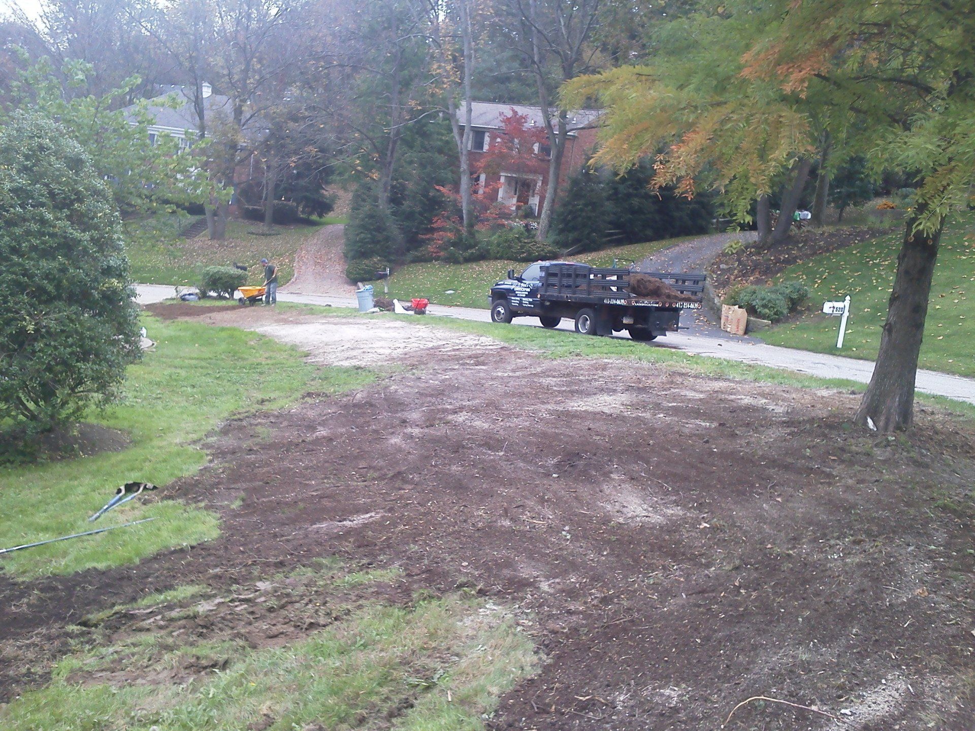 A truck is driving down a dirt road next to a house.