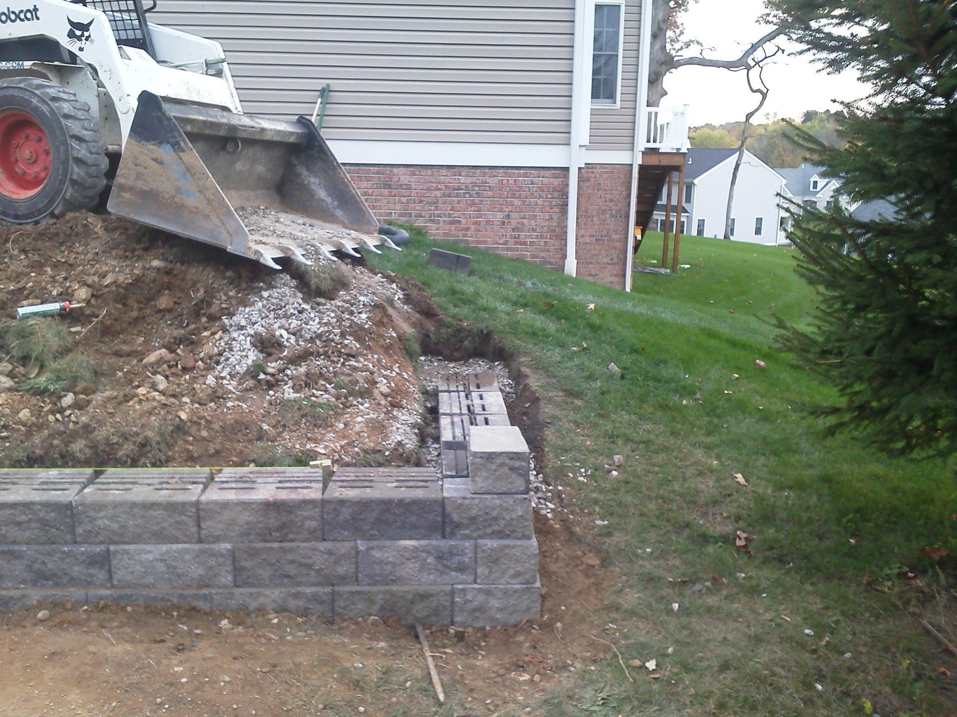 A bobcat tractor is working on a wall in front of a house
