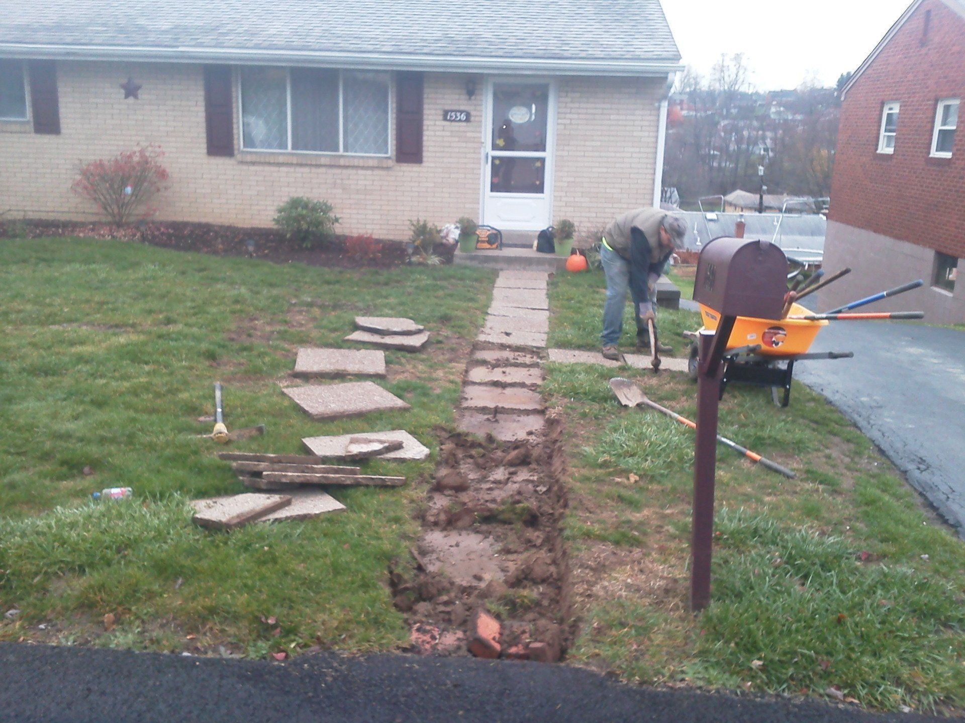 A man is working on a sidewalk in front of a house