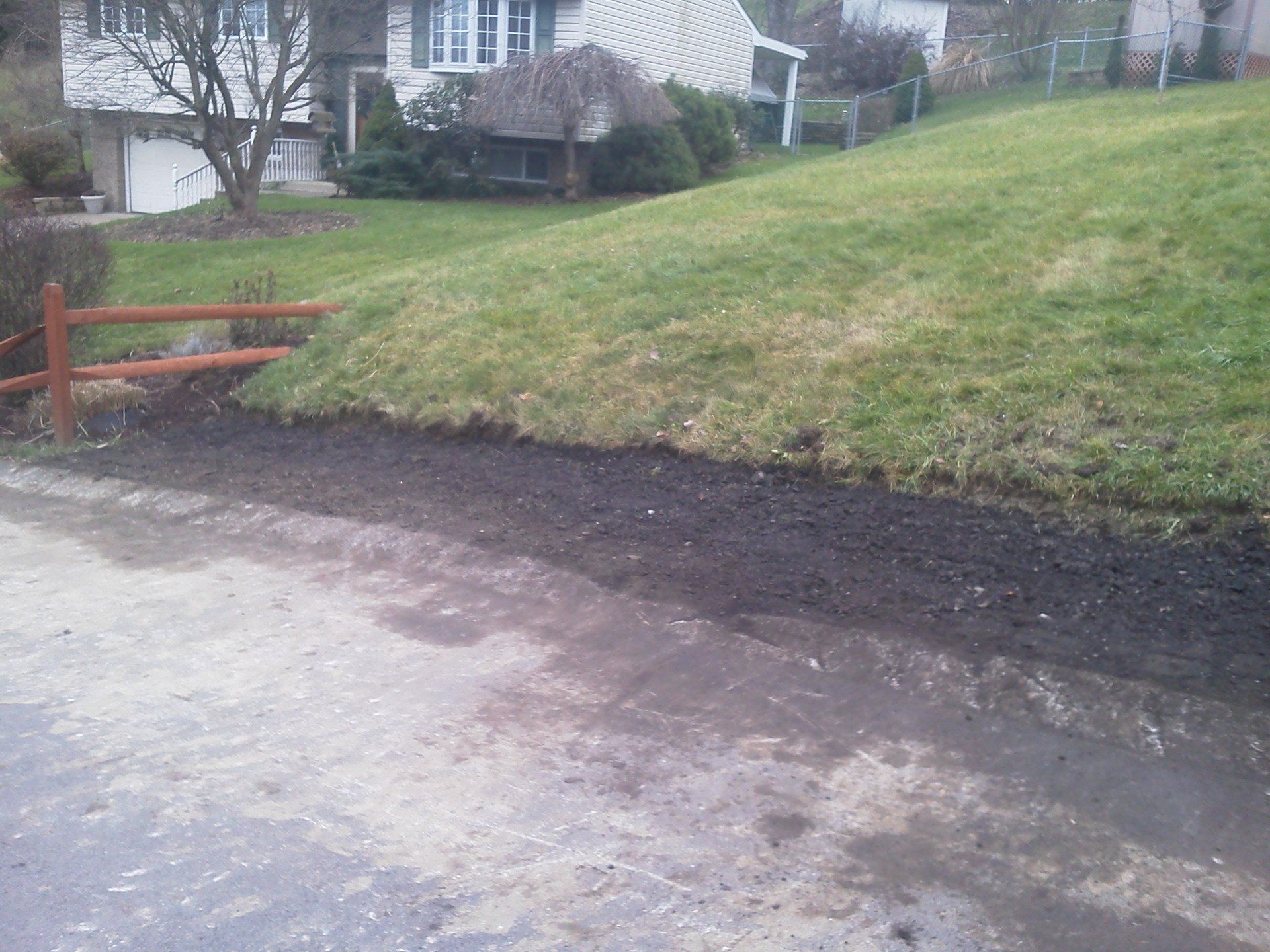A wooden fence is surrounded by grass and dirt in front of a house.