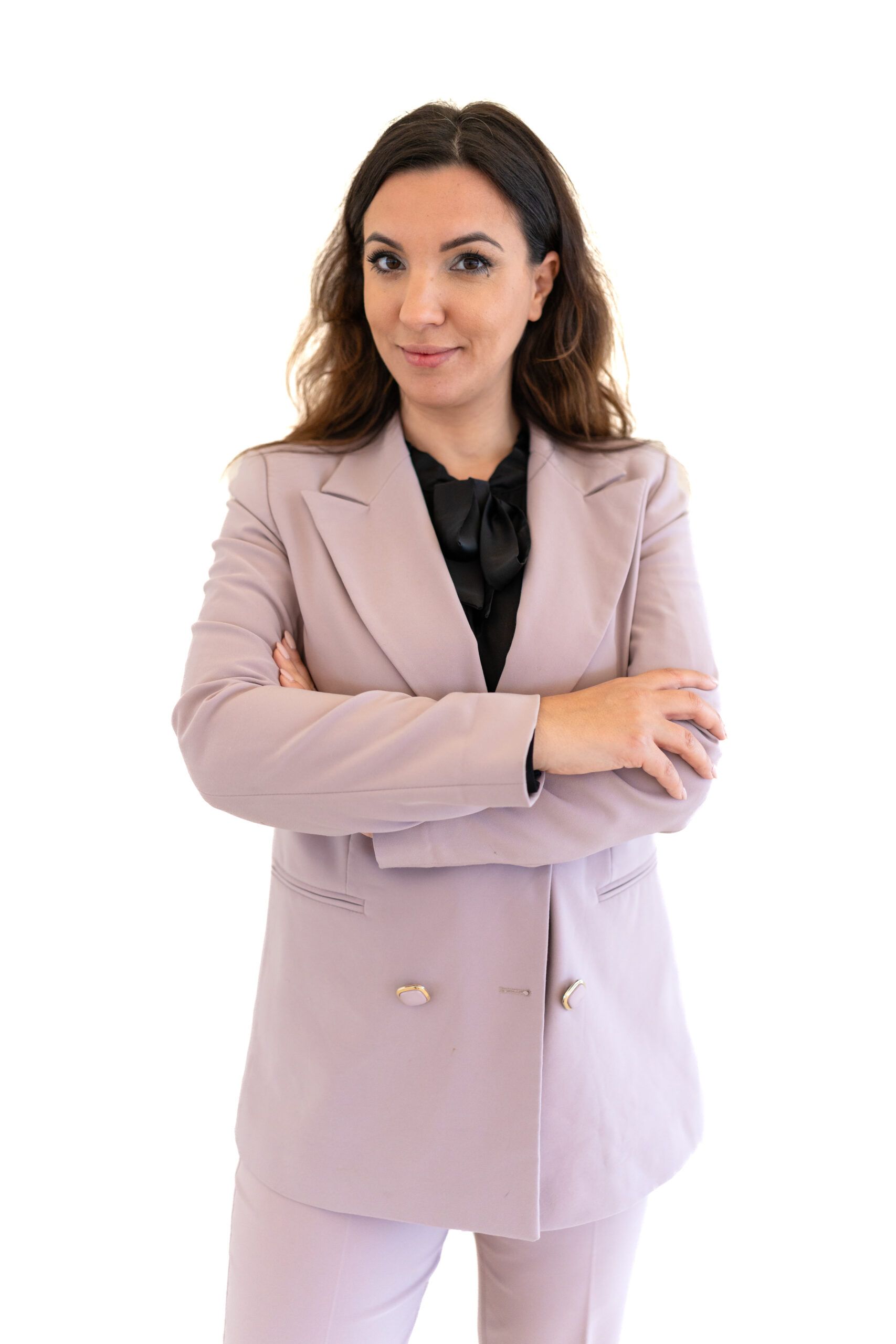 Donna con blazer rosa chiaro in piedi con le braccia incrociate su sfondo bianco
