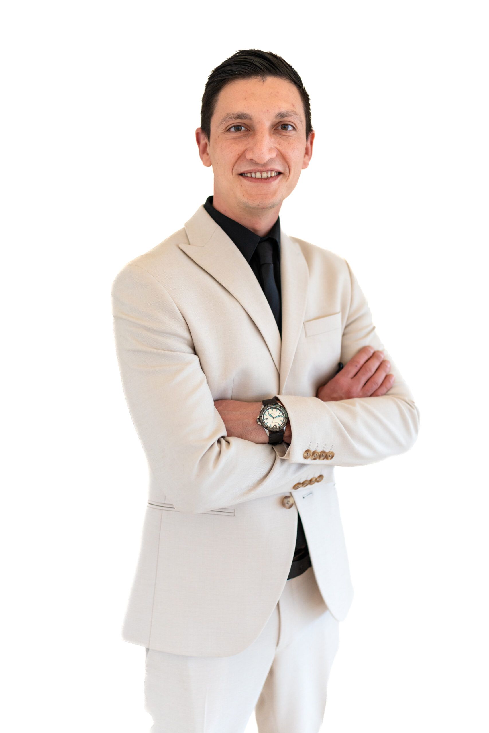 Uomo con blazer beige chiaro, braccia incrociate, sorridente su sfondo bianco.