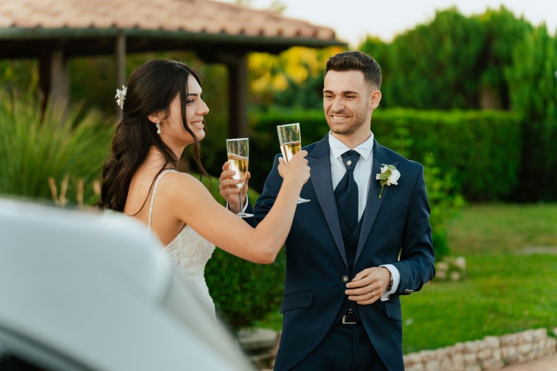 Una coppia in abito formale brinda con champagne all'aperto durante un ricevimento di nozze in giardino.