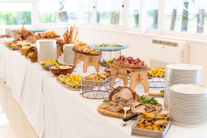 Un tavolo da buffet con un assortimento di cibi per la colazione, pasticcini, frutta e piatti bianchi impilati in una stanza luminosa.