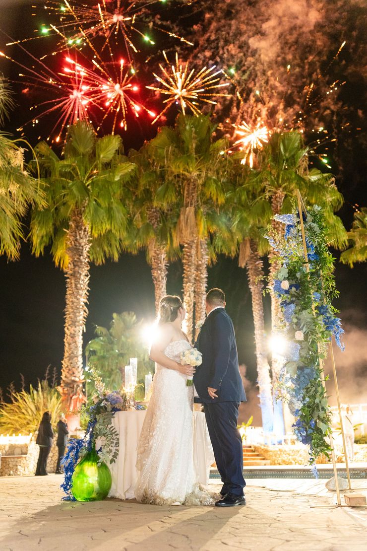 Gli sposi novelli sotto le palme, con i fuochi d'artificio che illuminano il cielo notturno.