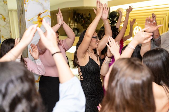 Persone che ballano con le braccia alzate in una scena di festa al chiuso e affollata