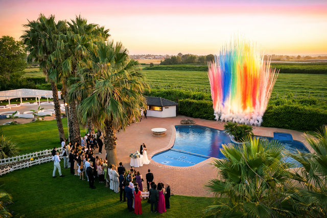 Festa all'aperto a bordo piscina al tramonto, con gli ospiti che ammirano una colorata fontana verticale.