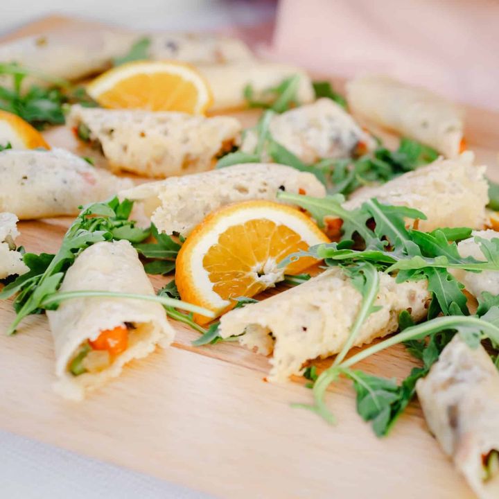 Involtini di rucola e agrumi serviti su un tagliere di legno, con fette d'arancia.