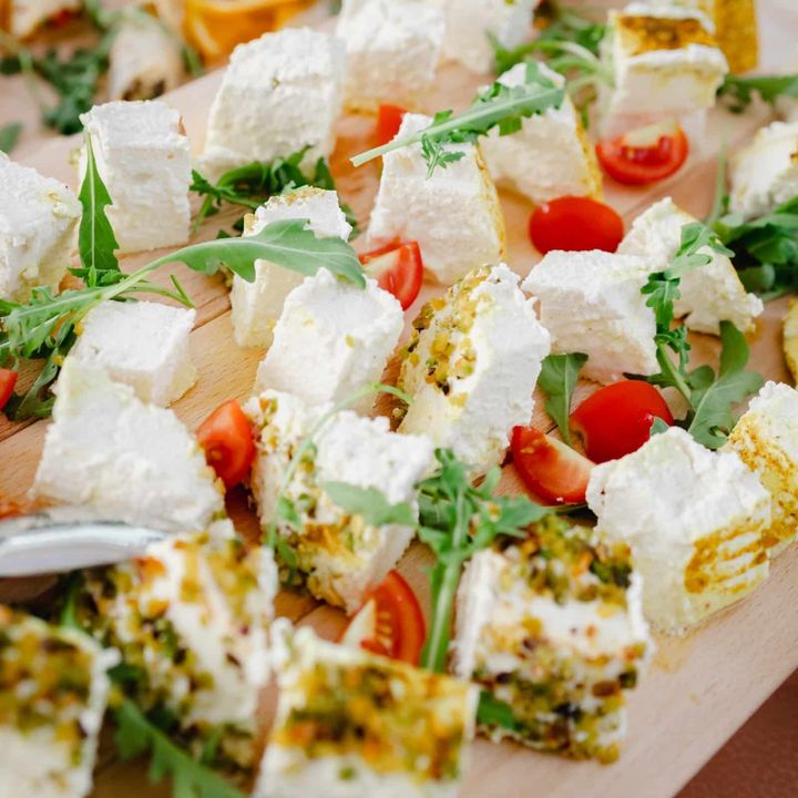 Piatto di cubetti di antipasto con feta, rucola e pomodorini, su un vassoio bianco.
