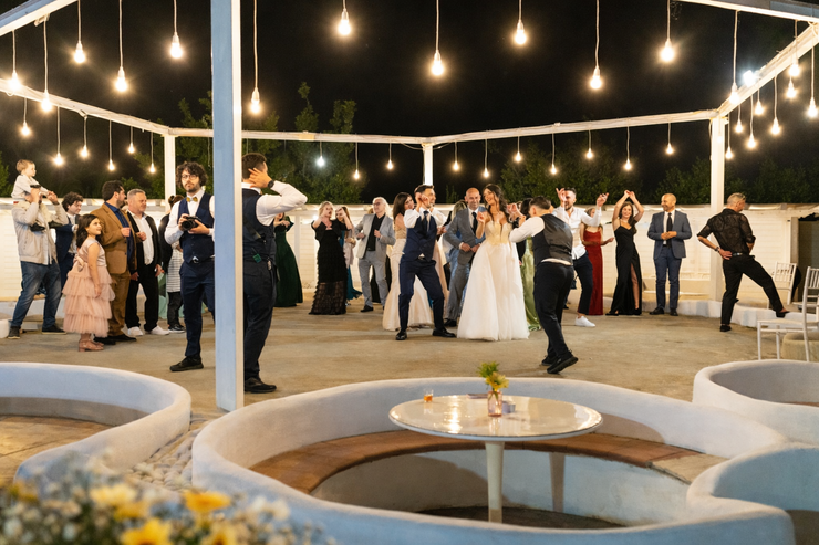 Gli invitati al matrimonio ballano sotto le luci decorative intorno agli sposi all'aperto di notte.