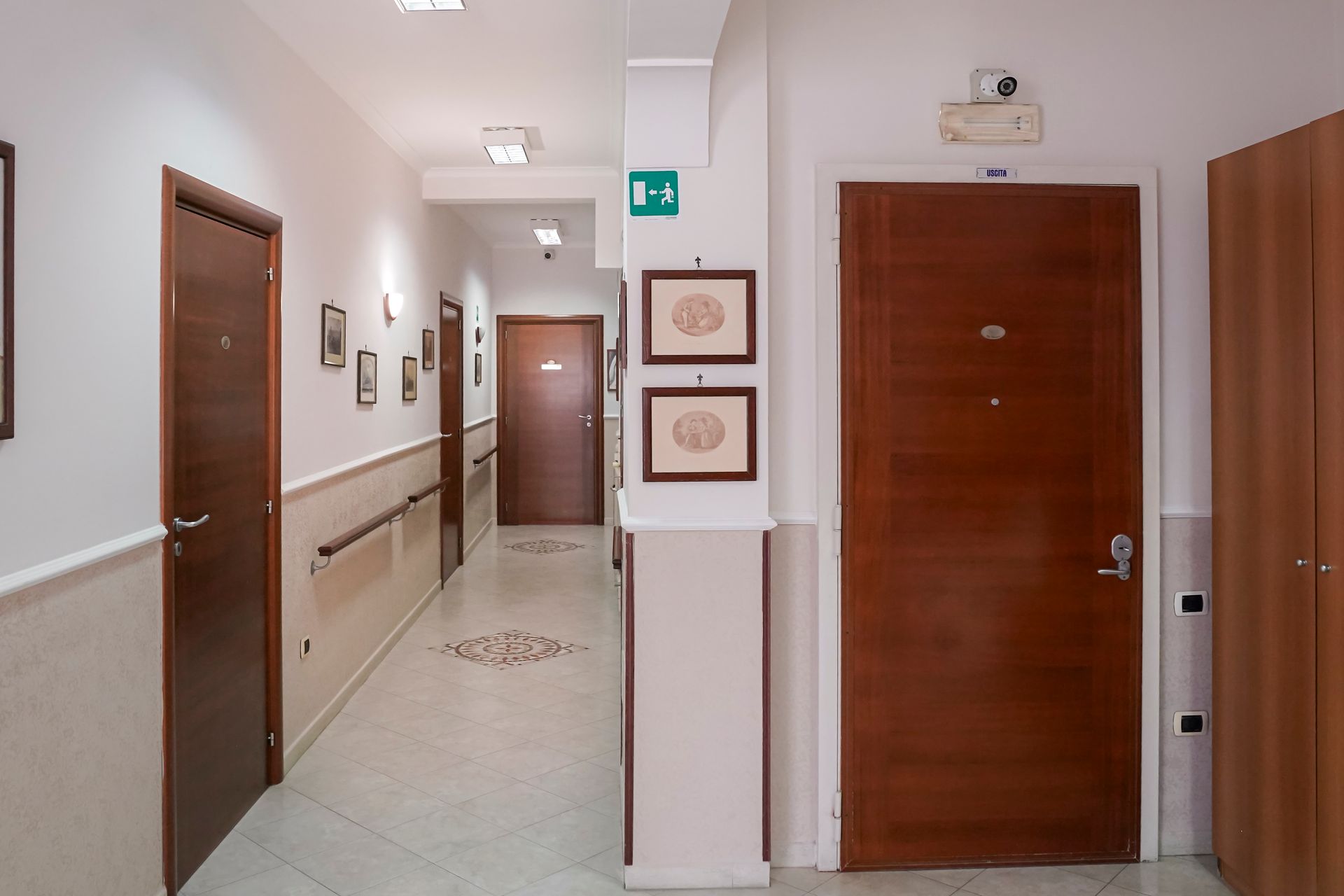Un lungo corridoio con porte di legno e un cartello verde di uscita sul muro.