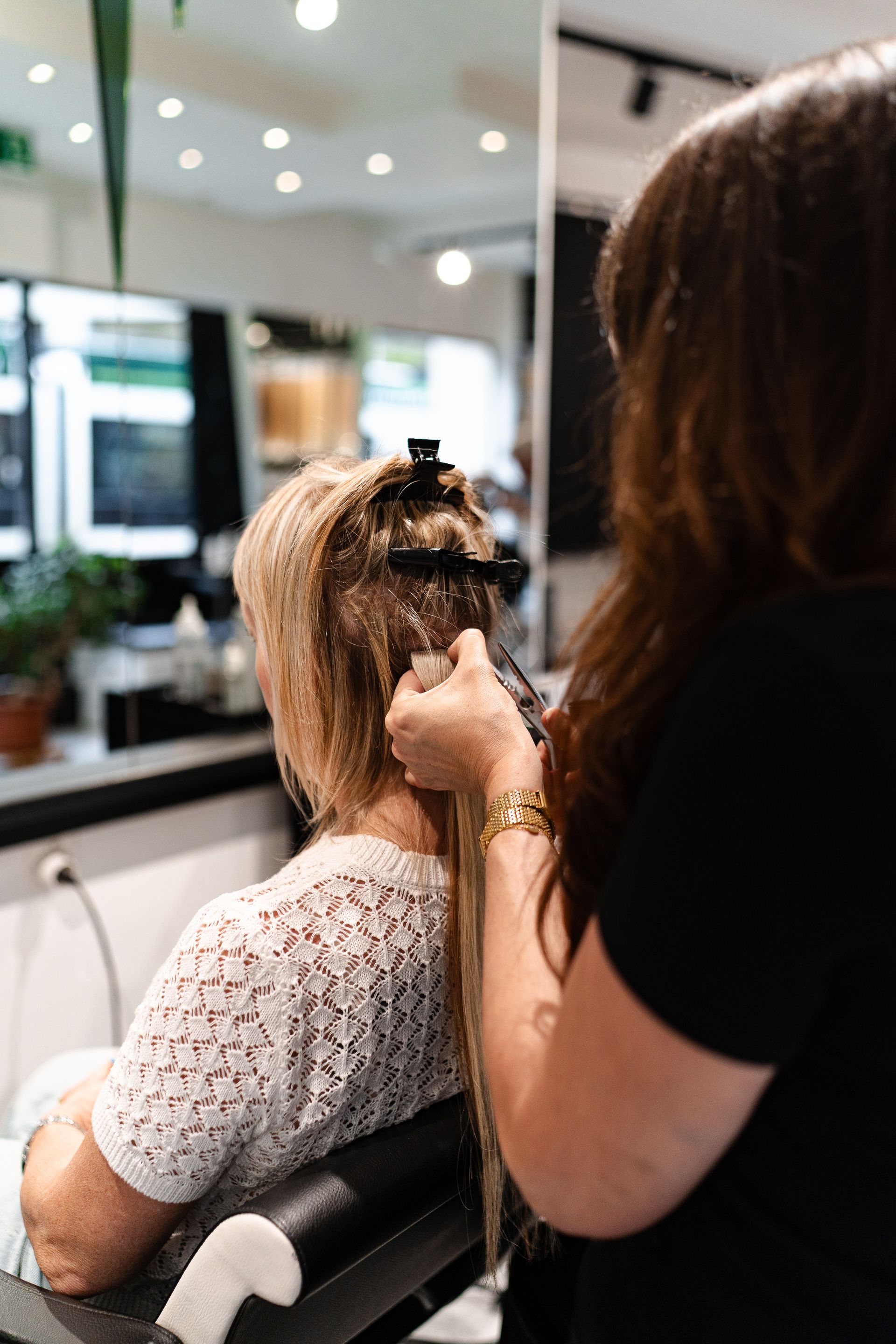Une personne blonde aux cheveux ondulés porte un blazer gris sur un fond clair uni et regarde directement l'objectif.