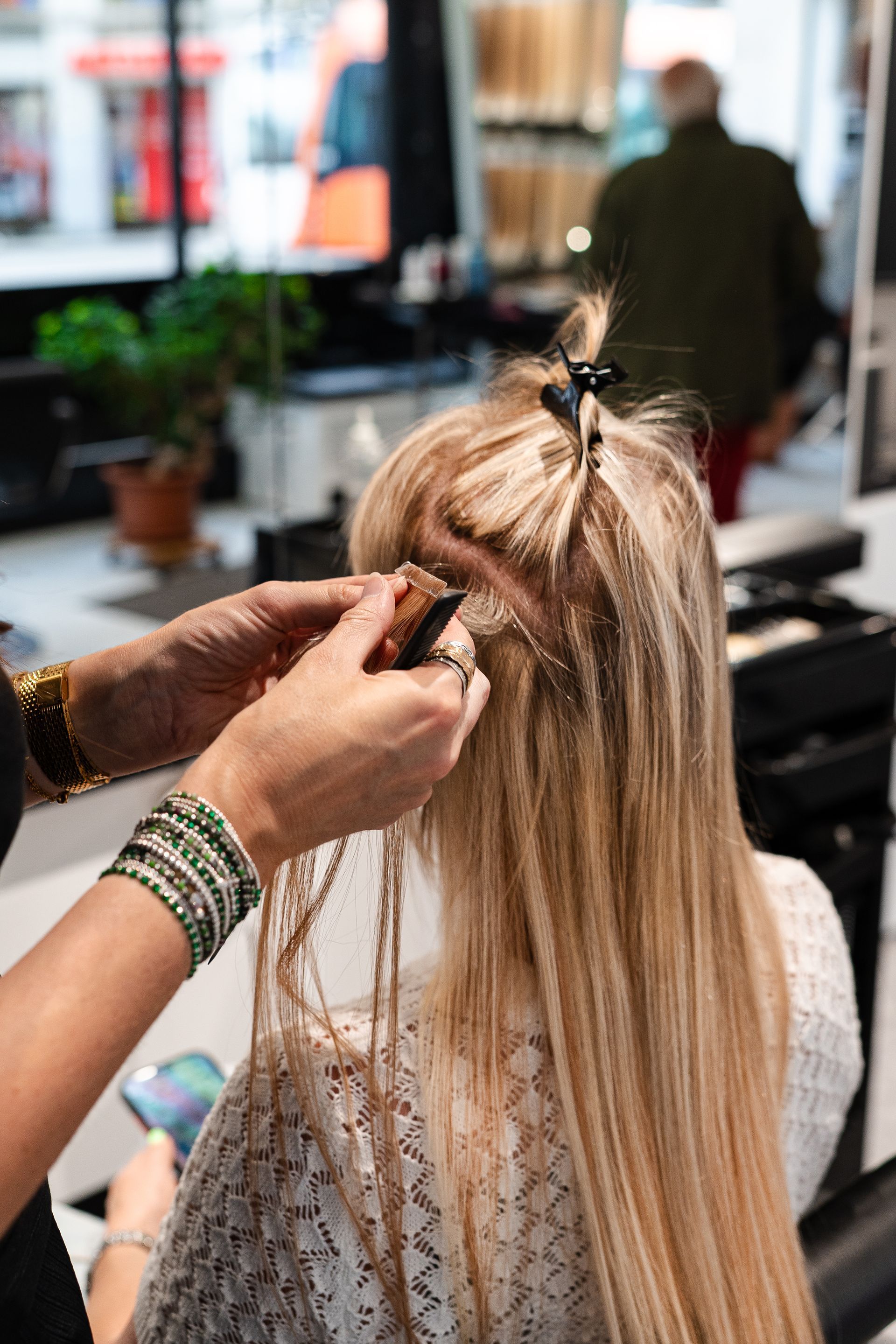 Personne souriante aux cheveux blonds et aux bras levés, se détachant sur un fond rose uni.