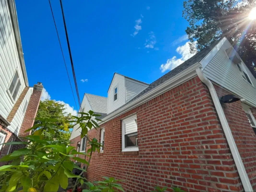 A brick house exterior featuring multiple gabled dormer windows under a vibrant blue sky with bright sunlight.