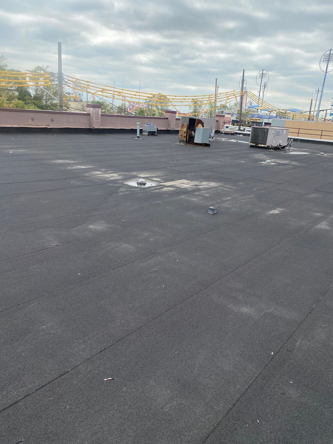 A wide-angle shot of a flat, dark gray industrial roof under a cloudy sky, with several HVAC units in the background.