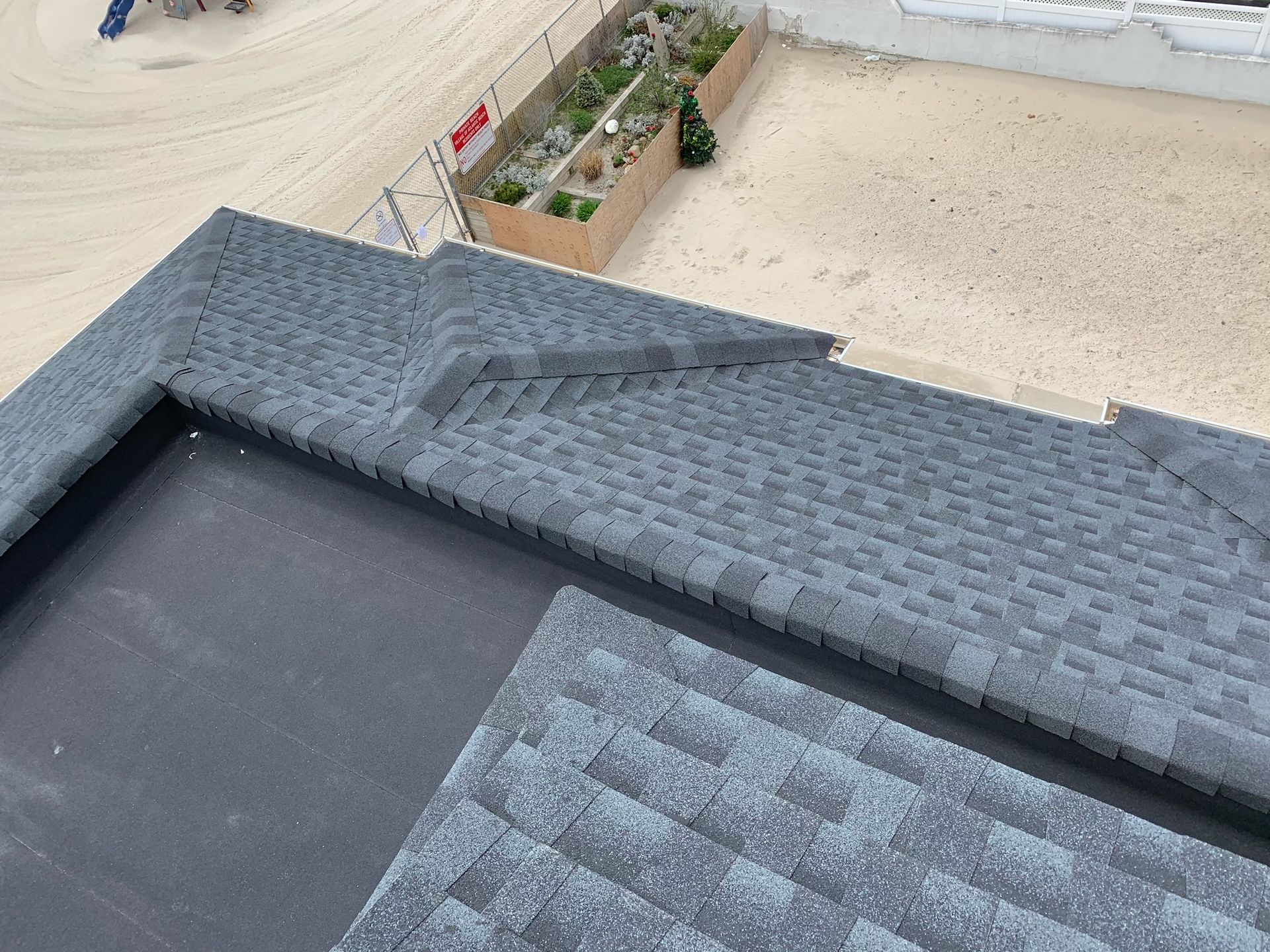 A view from above showing a dark gray shingled roof transitioning to a flat, dark membrane roof section.