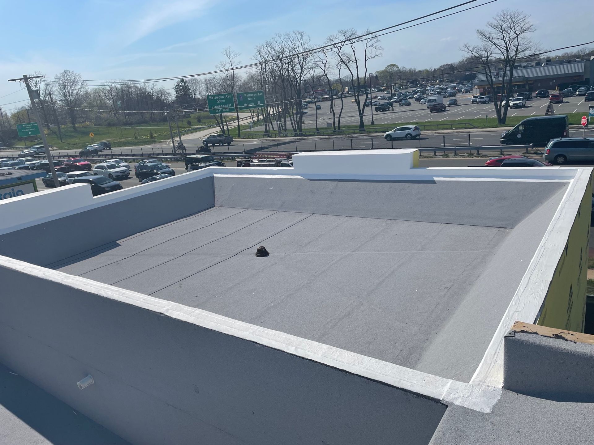 A high-angle view of a flat, gray commercial roof featuring a central drain and bright white perimeter parapet walls.