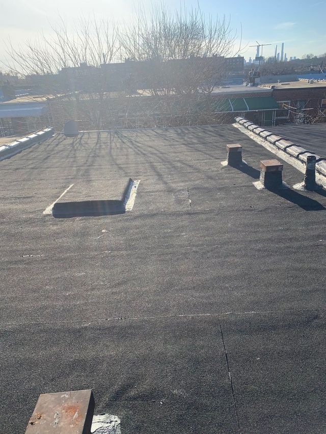 A flat, black-surfaced rooftop with several small square vents and a raised edge, under a bright, sunny sky.