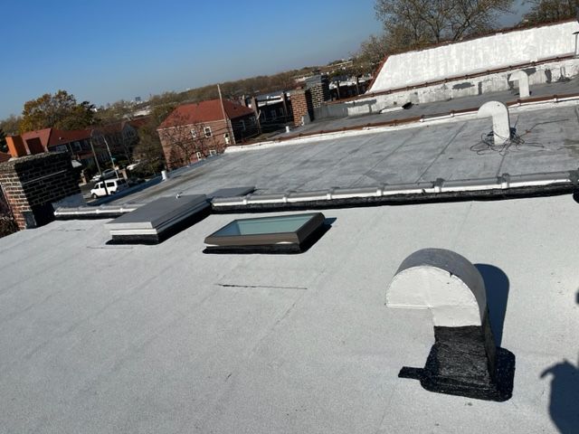 A flat, light-gray rooftop with two skylights and several ventilation pipes under a clear blue sky.