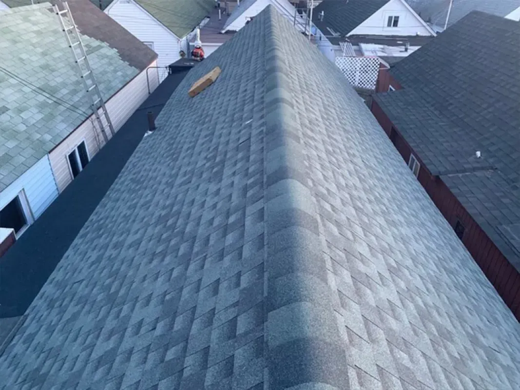 A high-angle view of a newly shingled gray roof peak with a small scrap of wood resting on the slope.