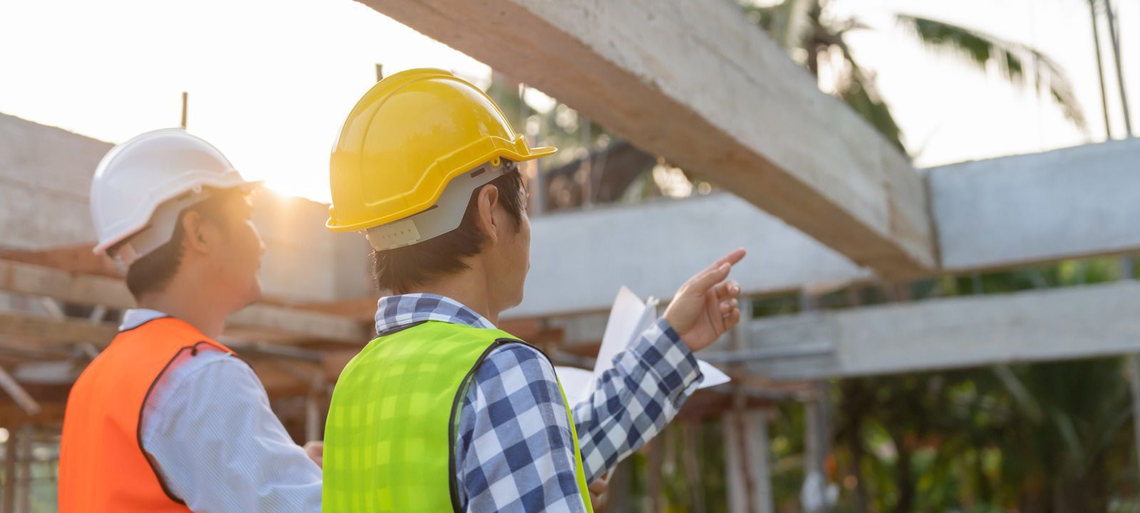 Two construction workers are looking at a blueprint at a construction site.