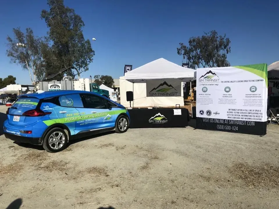 A blue car is parked in a dirt lot next to a tent.