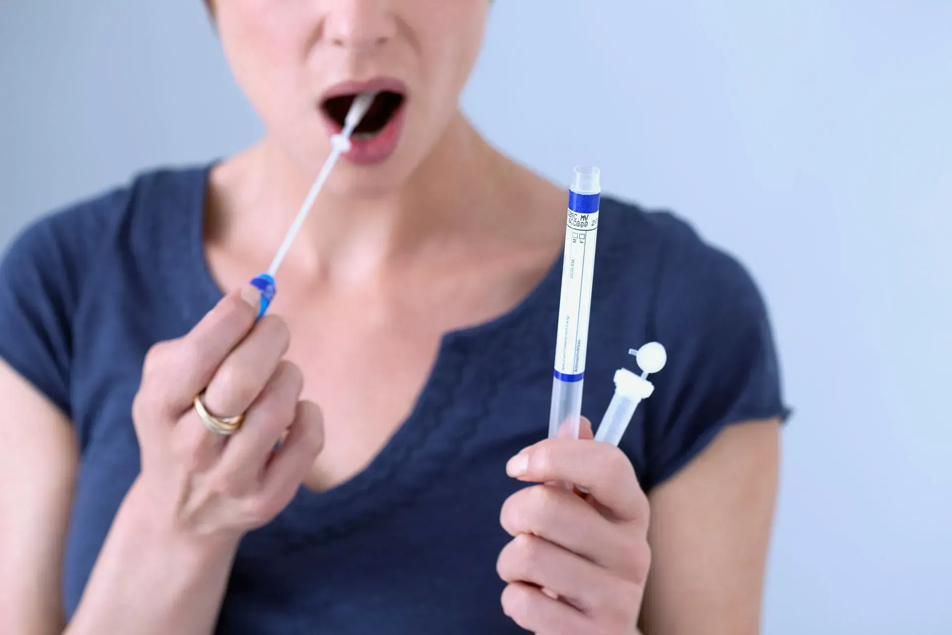 A woman is taking a sample from her mouth with a swab.