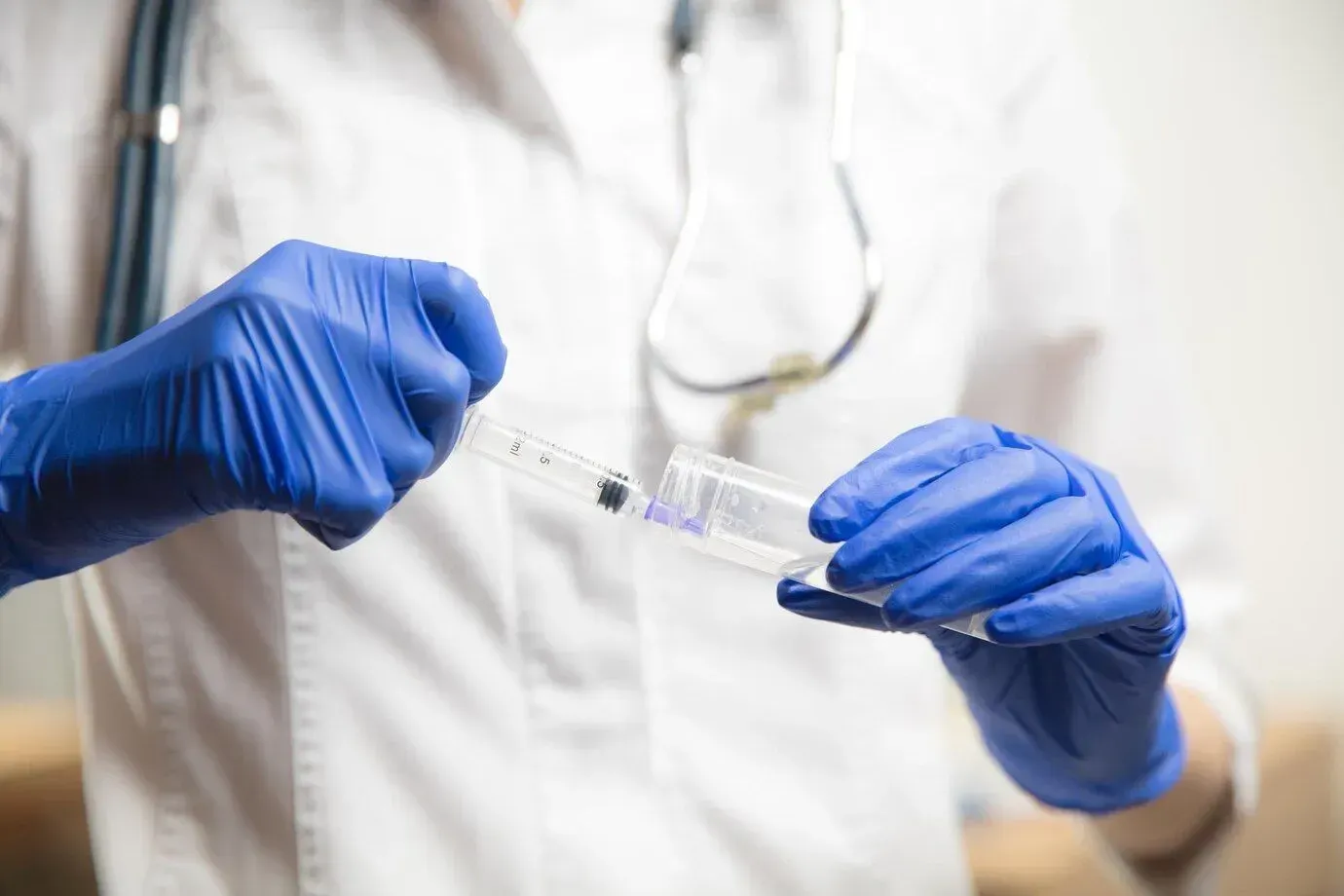 A doctor wearing blue gloves is holding a syringe.